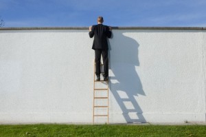Businessman on ladder looking over wall